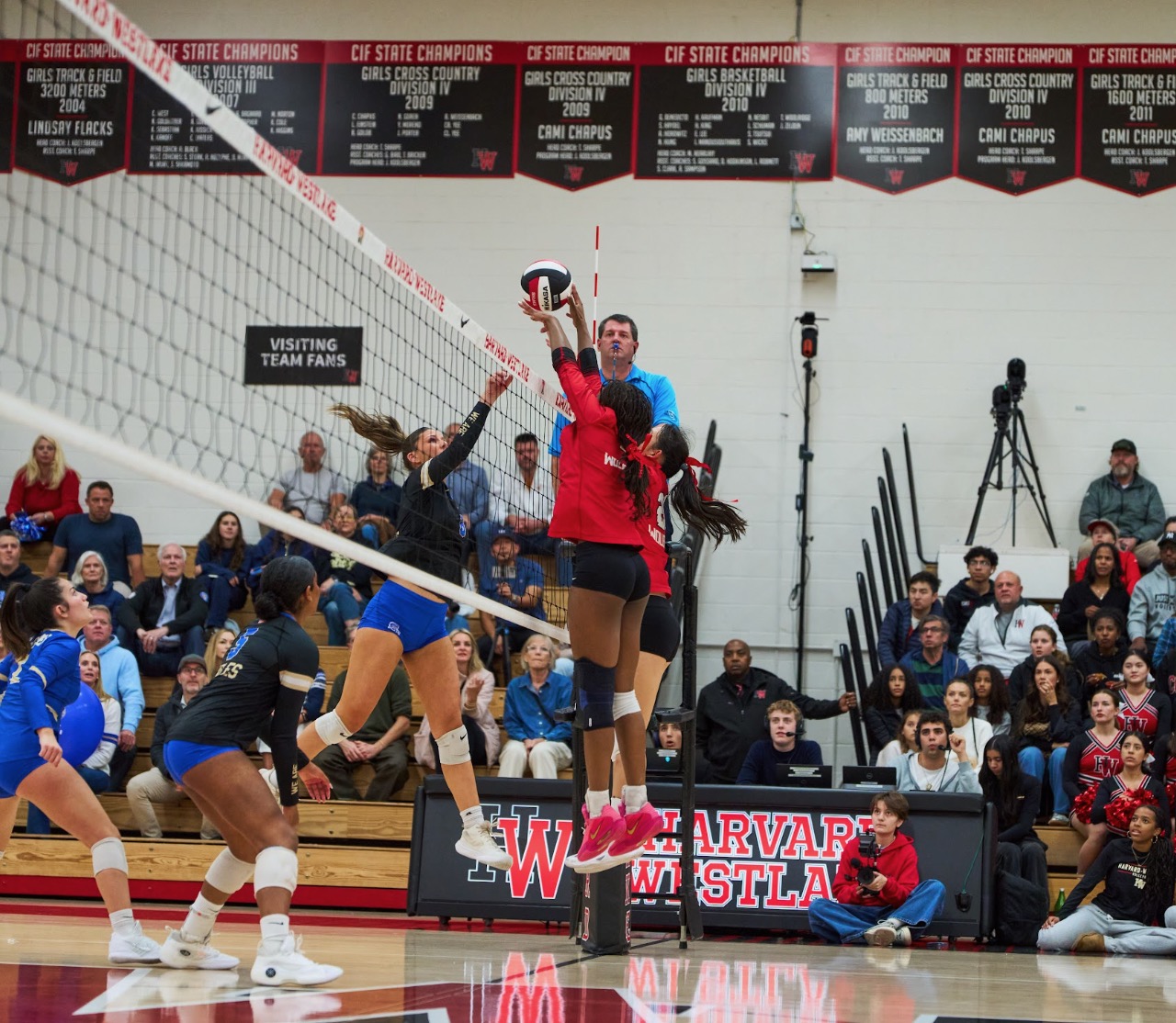 Lauryn Lewis blocking at the net in her red Harvard-Westlake jersey beneath the CIF State champion banners.