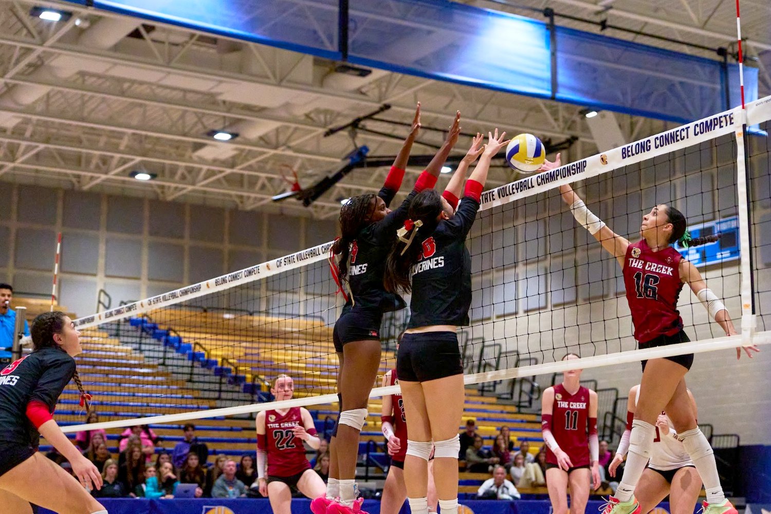 Lauryn Lewis and a teammate forming a double block at the net against an opposing hitter.