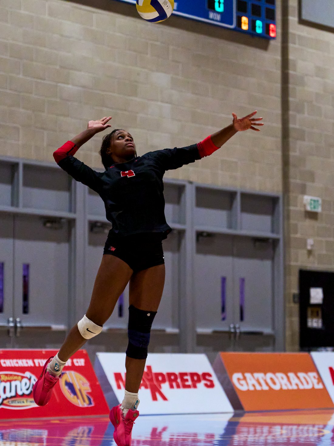 Lauryn Lewis airborne on a serve in front of the championship scoreboard.