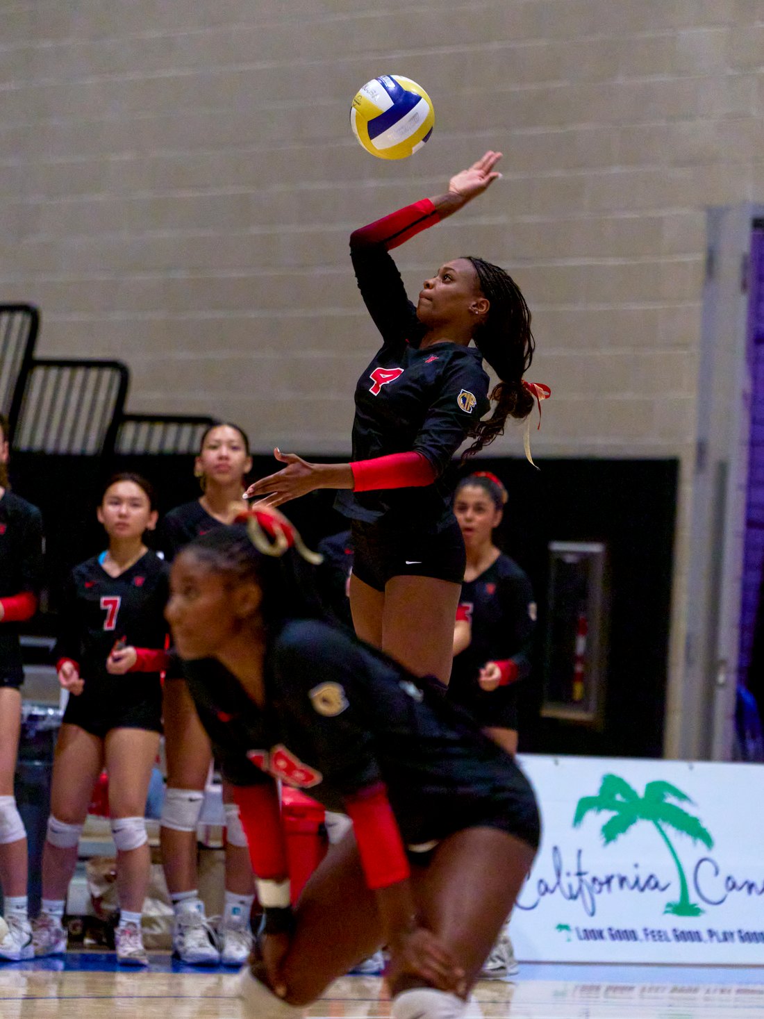 Lauryn Lewis jump serving, arm extended toward the ball above her.
