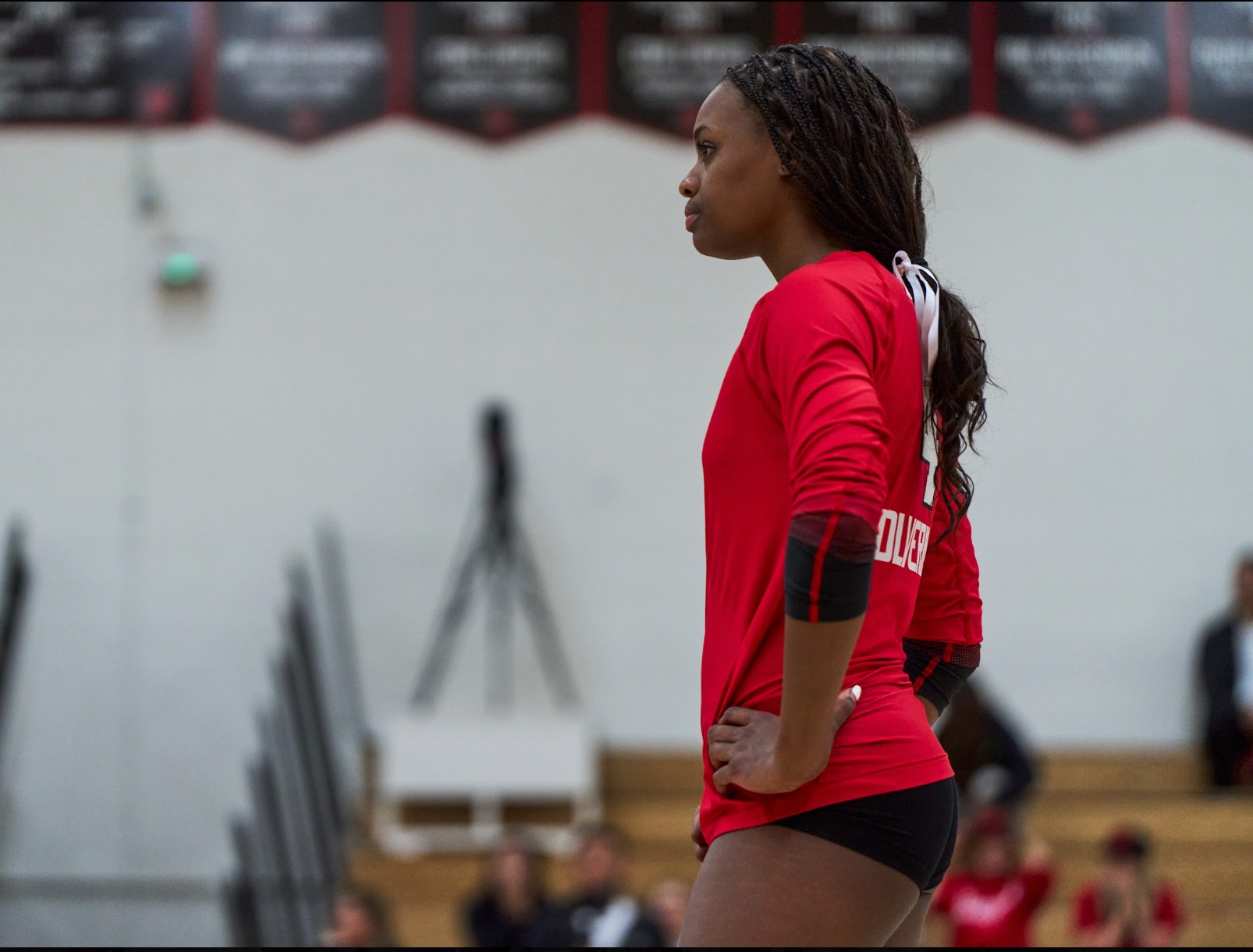 Lauryn Lewis standing in her red Harvard-Westlake jersey between points, watching the far court.